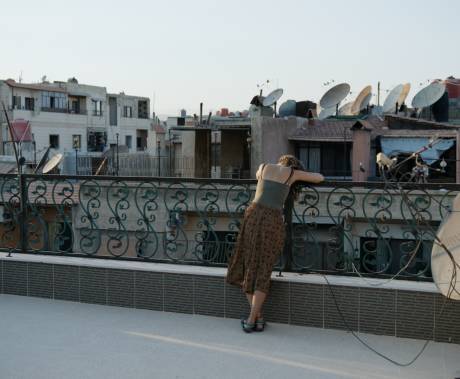 žena opírající se o zábradlí na terase, v pozadí domy