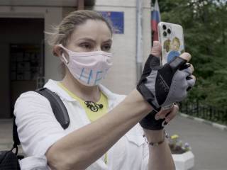 žena s rouškou přes ústa hledí do telefonu