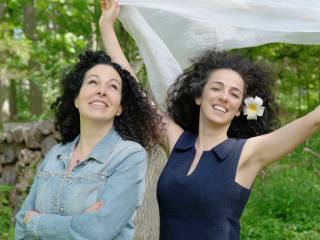 dvě ženy v lese, jedna nad hlavou drží šátek