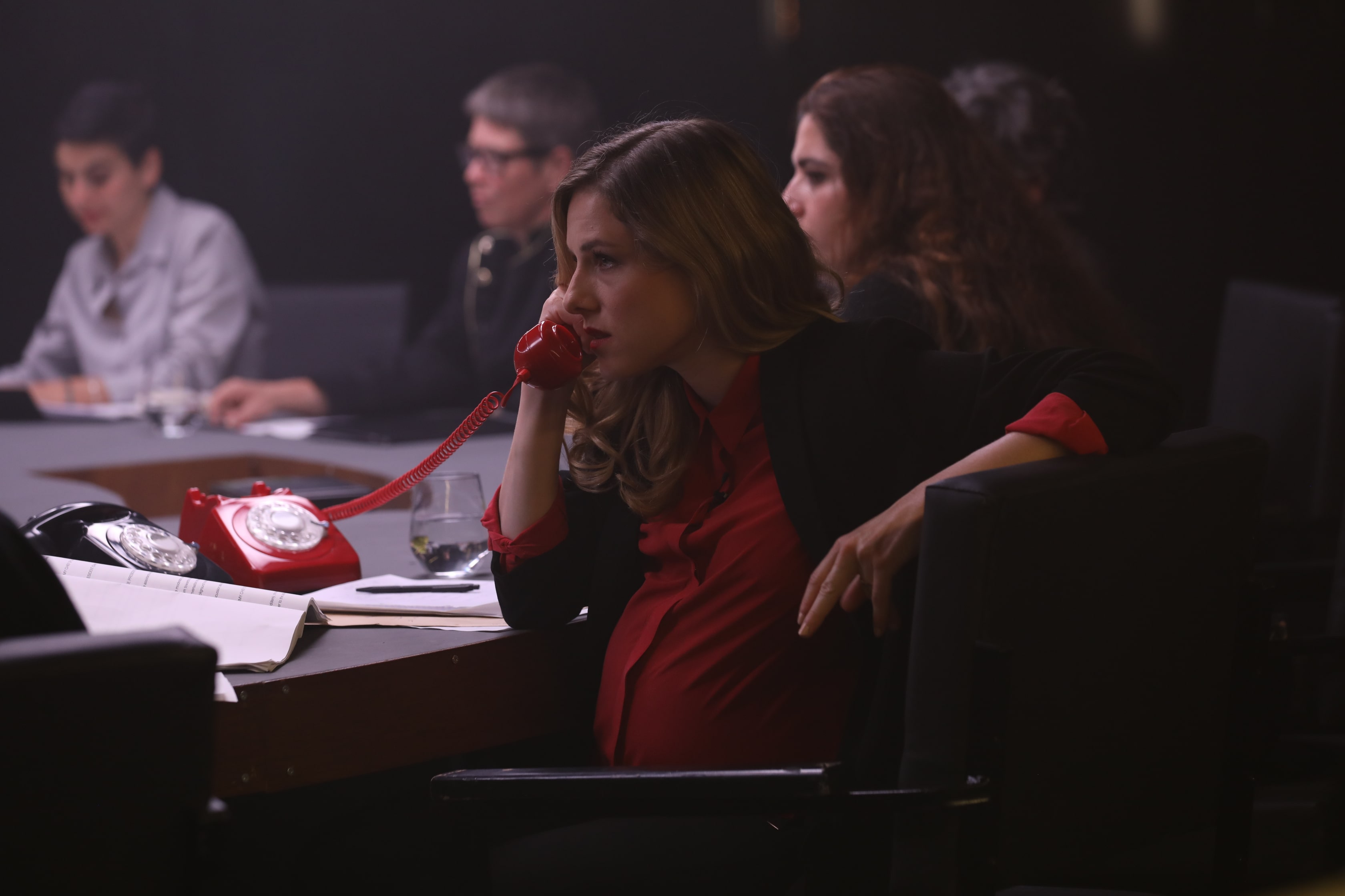 žena sedí u stolu s dalšími lidmi a telefonuje